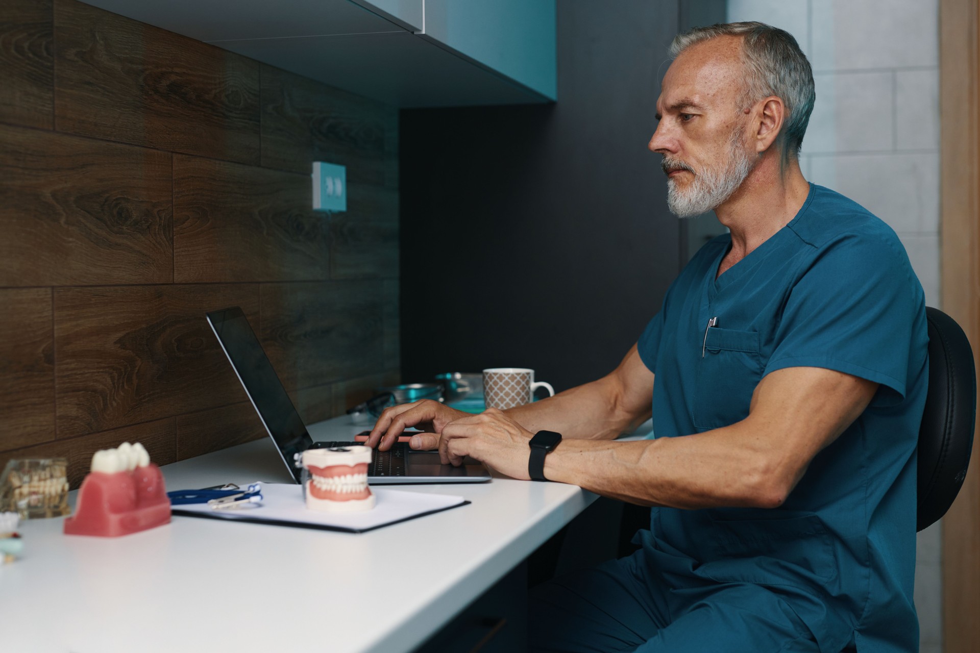 Working Senior Doctor in Blue Scrubs Using Laptop